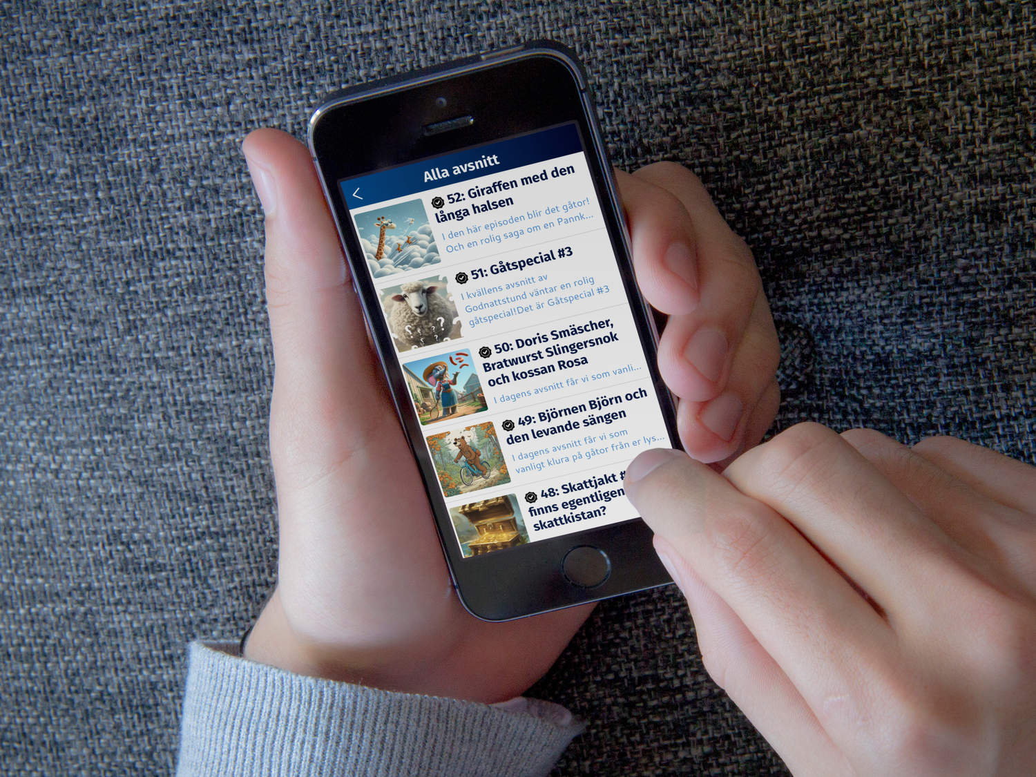 Två händer håller en mobiltelefon med Godnattstund-appens avsnittslista: Giraffen med den långa halsen, Gåtspecial och fler avsnitt